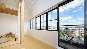 A spacious balcony with a table and chairs, a view of the cityscape, and a large window with black frames. - Super Spacious Penthouse in Art Deco Warehouse Conversion (London)