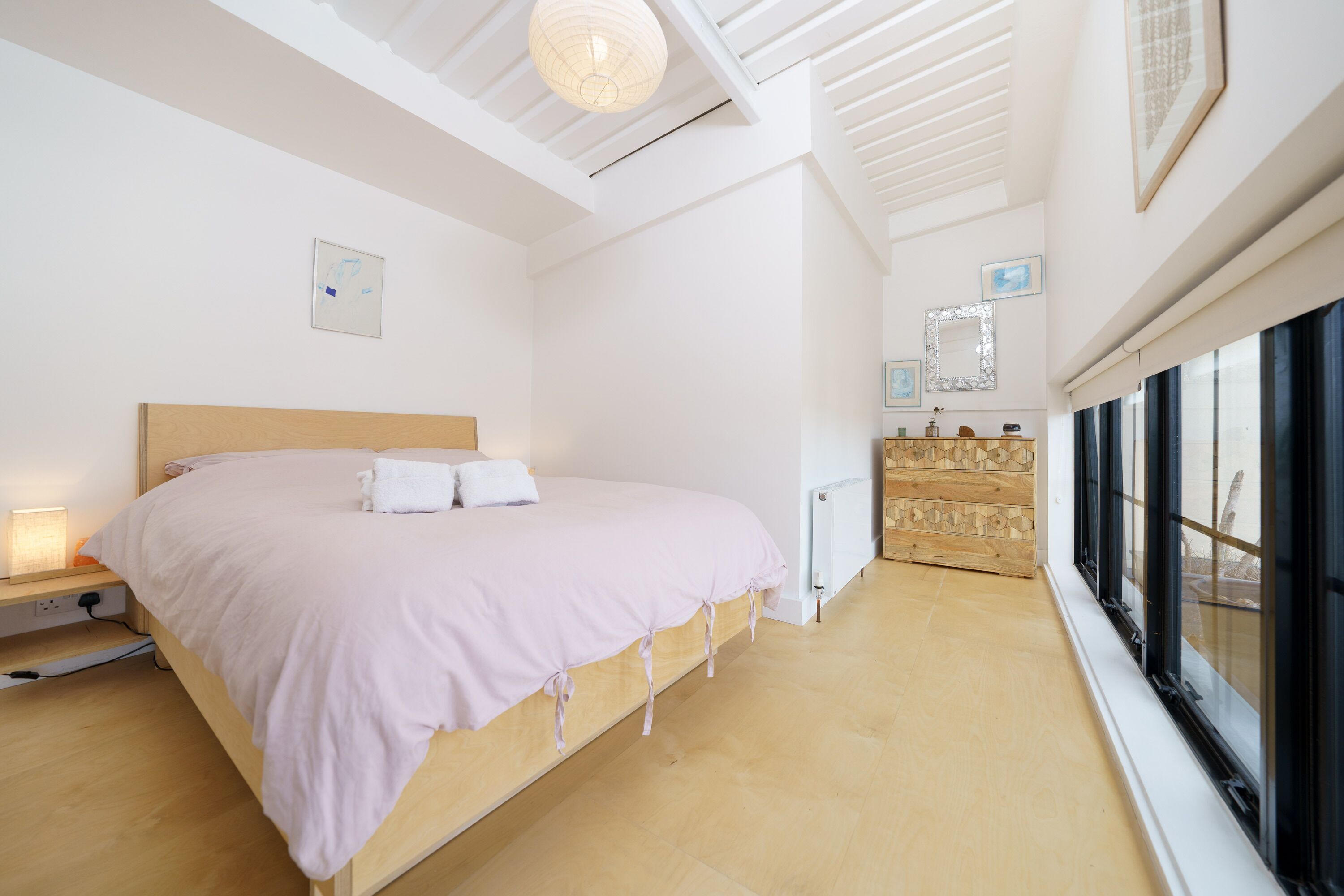 A bedroom with a wooden bed, a nightstand, a dresser, and a large window.