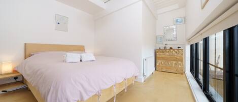 A bedroom with a wooden bed, a nightstand, a dresser, and a large window.