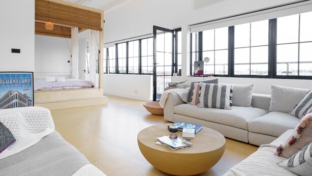 A modern living room with a large window, a round coffee table, and a sofa. - Super Spacious Penthouse in Art Deco Warehouse Conversion (London)