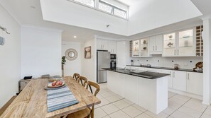 A modern kitchen with white cabinetry, a central island, and a dining area with a wooden table.