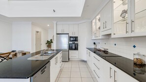 A modern kitchen with white cabinetry, a black countertop, and a stainless steel refrigerator.