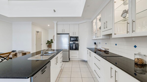 A modern kitchen with white cabinetry, a black countertop, and a stainless steel refrigerator.