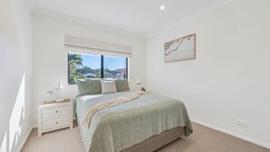 A bedroom with a bed, bedside tables, a window with a view, and a wall-mounted artwork.