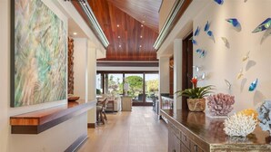 A spacious hallway with a wooden ceiling, a large abstract painting on the left, and a wall with colorful fish decorations. - Waiulu Estate 152B – Ocean View & Fully Renovated | Onsite Staff & Daily Housekeeping (Kailua Kona)