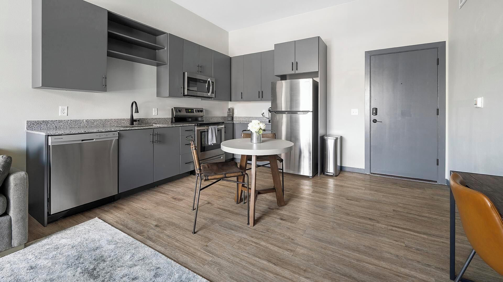 A modern kitchen with grey cabinets, stainless steel appliances, and a round dining table with chairs.