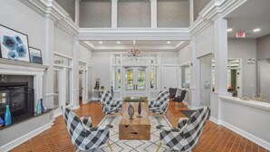 Een ruime lobby met een open haard, geruit gestoffeerde stoelen, een centrale tafel en een kroonluchter.