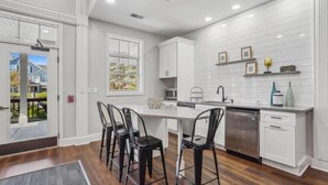 A modern kitchen with white cabinetry, a central island with bar stools, a dishwasher, and a microwave. - Landing | Stylish 2BD, Pool, Tennis Court (West Dundee)