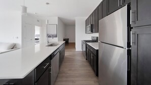Une cuisine moderne dotée d’appareils électroménagers en acier inoxydable, de meubles de rangement noirs et d’un plan de travail blanc.