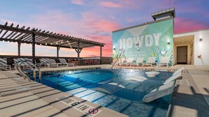 A rooftop pool with lounge chairs, a wooden pergola, and a mural advertising the hotel. - Landing | Spectacular 1BD, Courtyard, Gym (Austin)