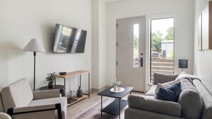 A modern living room with a sofa, armchair, coffee table, TV, and a door leading outside. - Landing | Stylish 1BD, Courtyard, Gym (Austin)