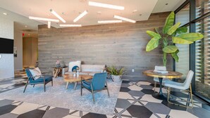 A modern lobby with a wooden wall, a large plant, and a seating area with a coffee table and chairs. - Landing | Stylish 1BD, Courtyard, Gym (Austin)