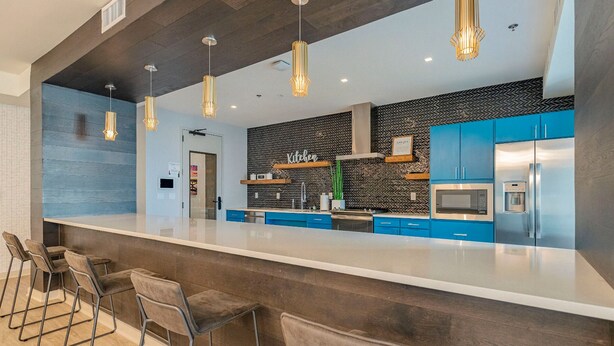 A modern kitchen with blue cabinets, a large island, and pendant lighting. - Landing | Stylish 1BD, Courtyard, Gym (Austin)