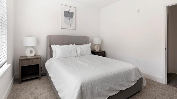 A bedroom with a bed, two bedside tables, a wall-mounted light, and a door.