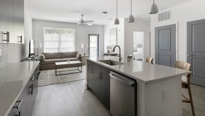 Een moderne keuken met een centraal eiland, inbouwapparatuur en een zithoek met een bank en salontafel.