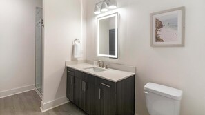 A bathroom with a glass shower enclosure, a vanity with a sink, a toilet, and a framed picture on the wall.
