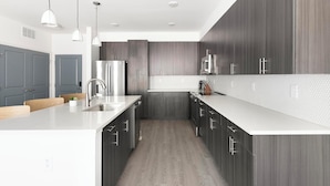 Een moderne keuken met donkere houten kastjes, witte aanrechtbladen en roestvrijstalen apparatuur.
