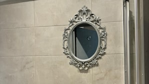 Un baño con un espejo grande, un lavamanos con artículos de aseo y un perchero para toallas.