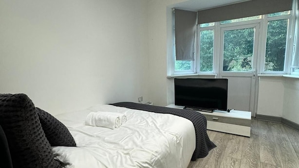 Un dormitorio moderno con cama, televisor de pantalla plana y ventana con vistas al verdor.