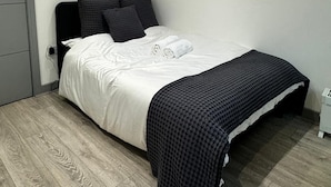 Un dormitorio con cama, un armario gris y una mesita de noche blanca.