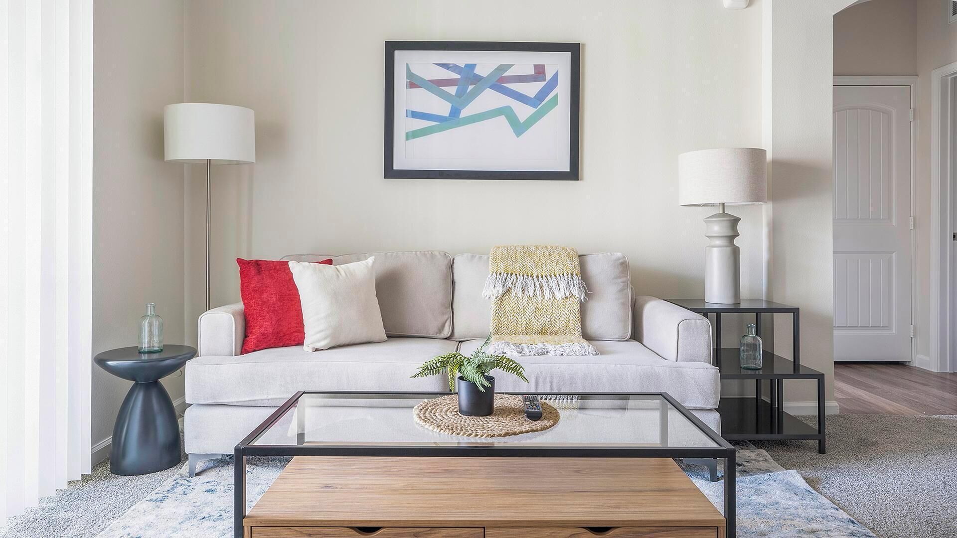 A living room with a sofa, two side tables, a coffee table, and a framed abstract painting.