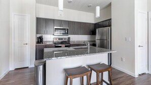 A modern kitchen with dark cabinets, stainless steel appliances, granite countertops, and a small bar area with stools. - Landing | Modern 1BD, Pool, Clubhouse (Pflugerville)