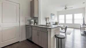 A modern kitchen with a built-in dishwasher, a coffee maker, and a sink. There is a dining area with a table and chairs, and a ceiling fan. - Landing | Chic 1BD, Clubhouse, Gym (Austin)