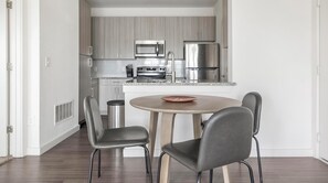 Une cuisine moderne dotée d’appareils électroménagers en acier inoxydable, d’une table ronde en bois et de deux chaises grises.