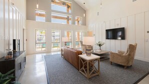 A spacious living room with a large window, a sofa, a coffee table, and a TV mounted on the wall. - Landing | Chic 1BD, Clubhouse, Gym (Austin)