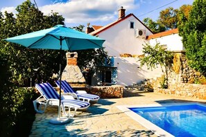 A swimming pool with lounge chairs and a blue umbrella, surrounded by stone walls and greenery. - Pictoresque pool villa (Hreljin)