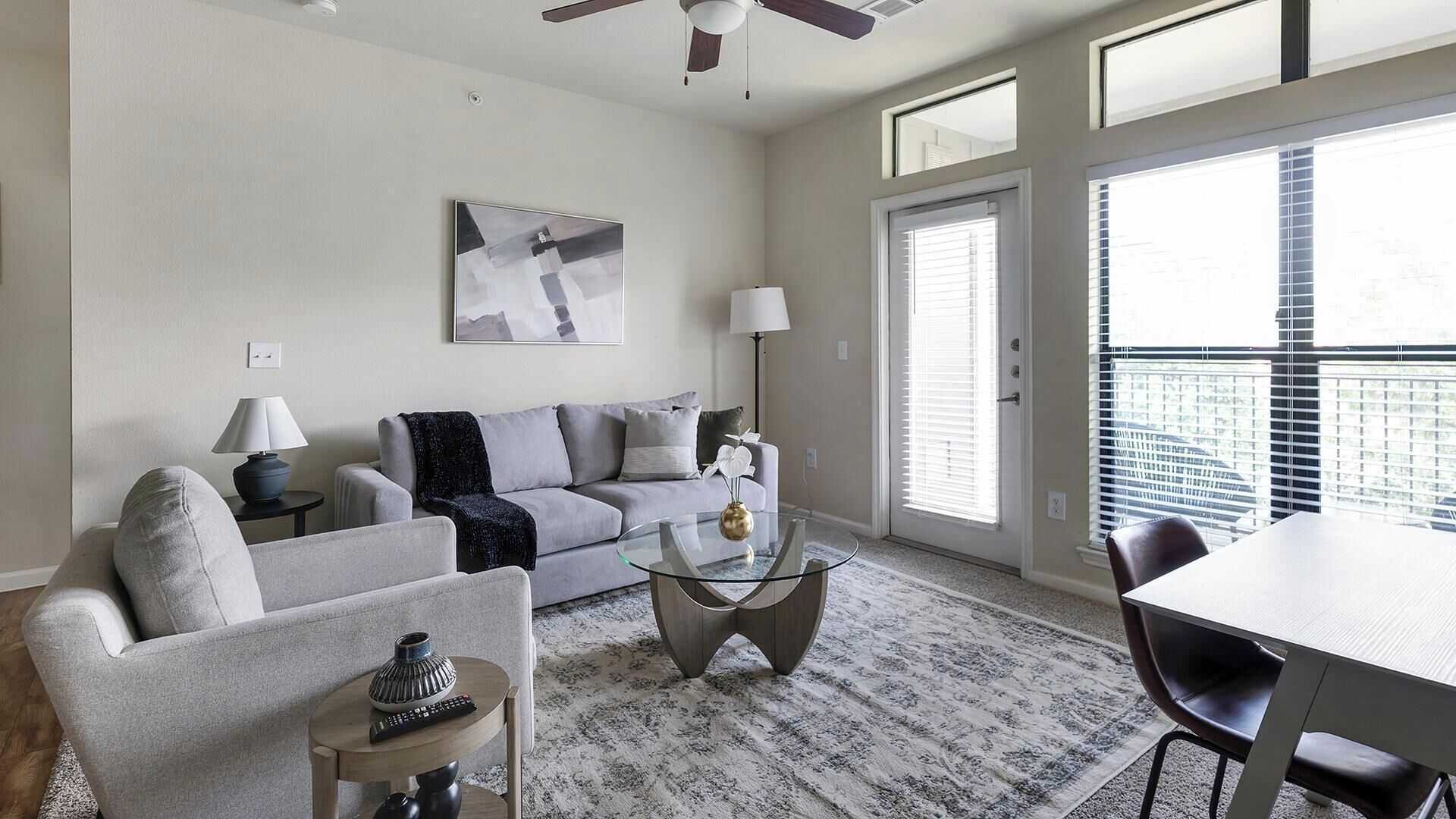 A modern living room with a grey sofa, a glass coffee table, and a dining area with a table and chairs.