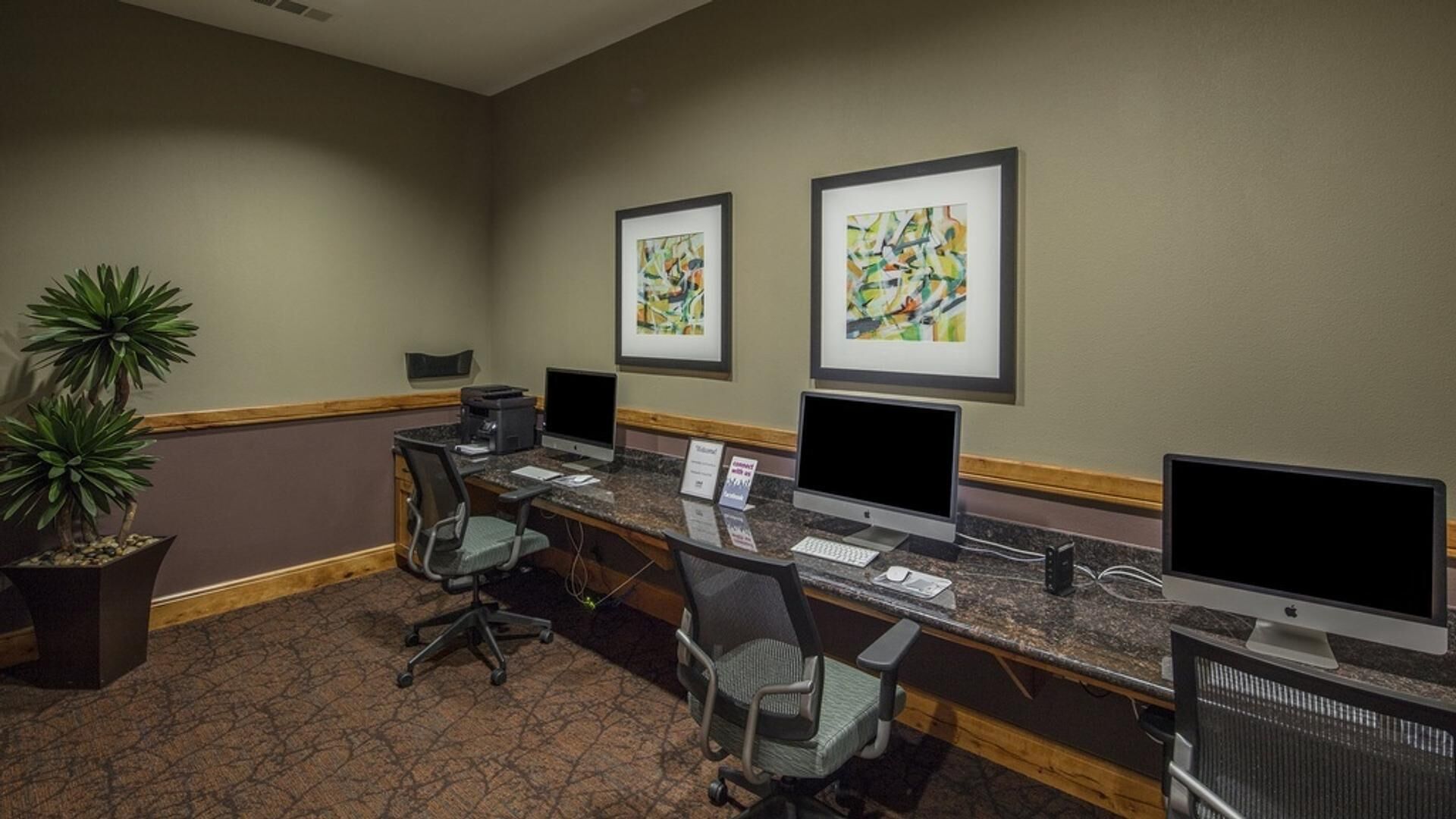 A reception area with three computer workstations, two chairs, a printer, and two framed abstract paintings on the wall.