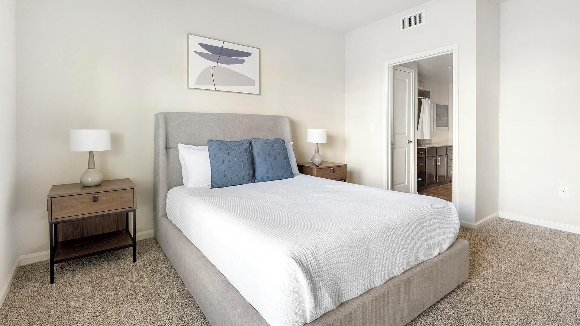 A neatly arranged bedroom with a large bed, two bedside tables, and a door leading to a bathroom.