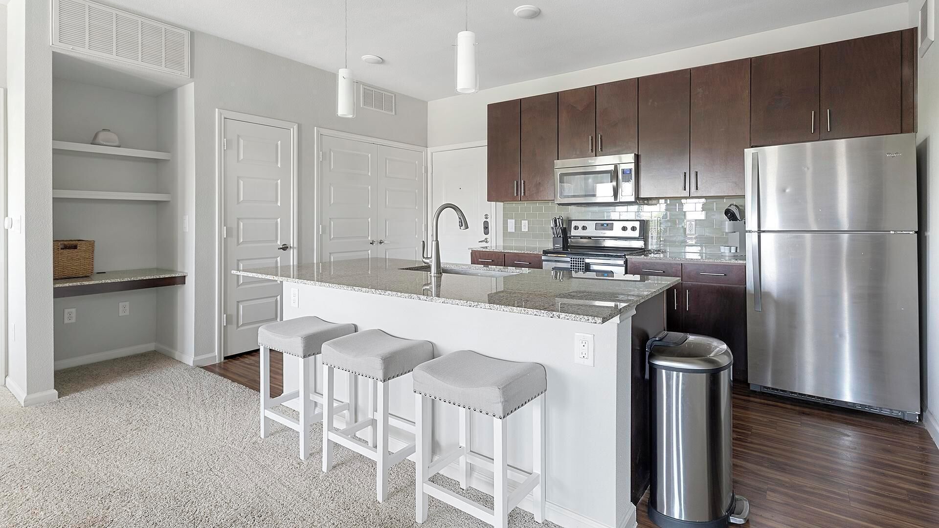 A modern kitchen with a central island, stainless steel appliances, and a trash can.