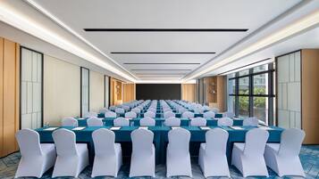 A conference room with rows of tables and chairs, large windows, and a modern ceiling design.
