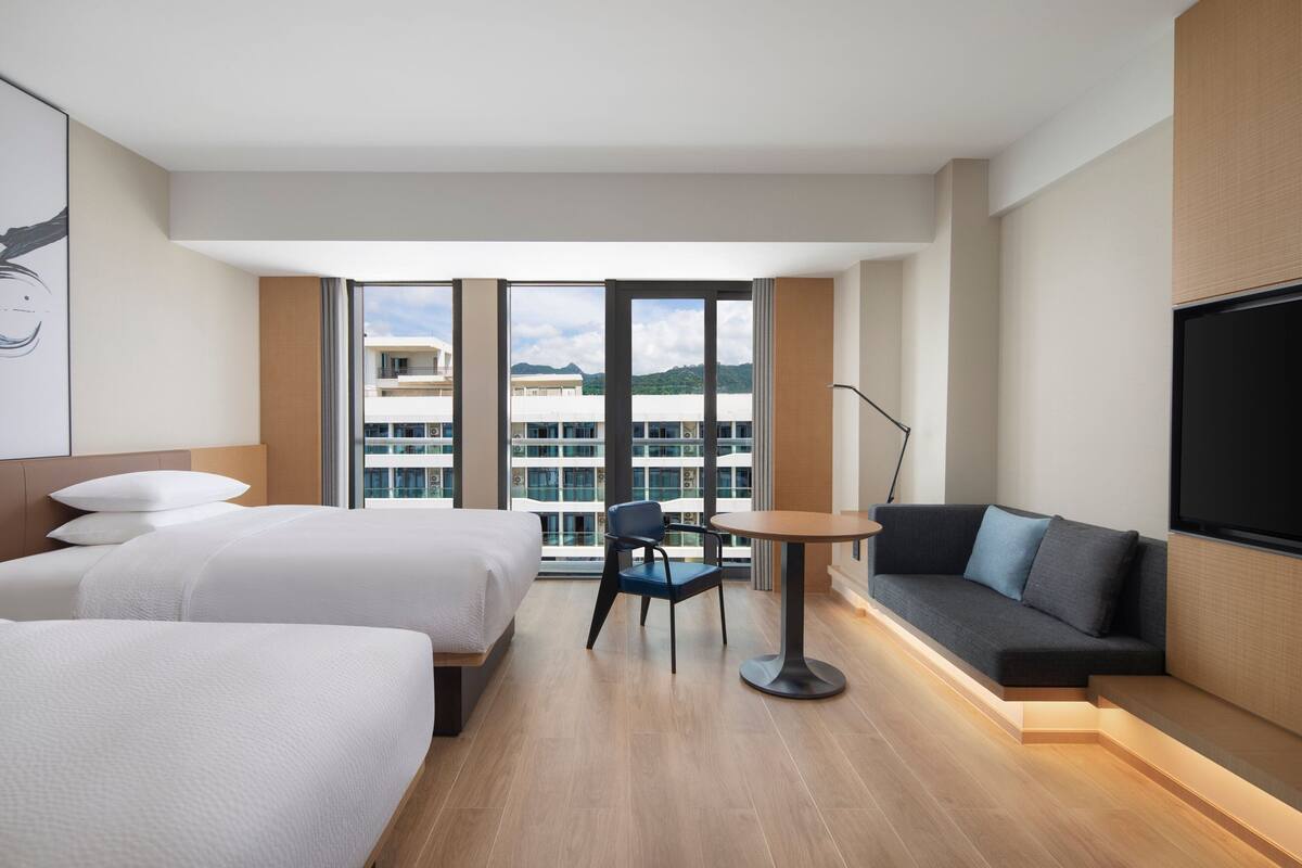 A hotel room with two beds, a sofa, a small table, and a TV.
