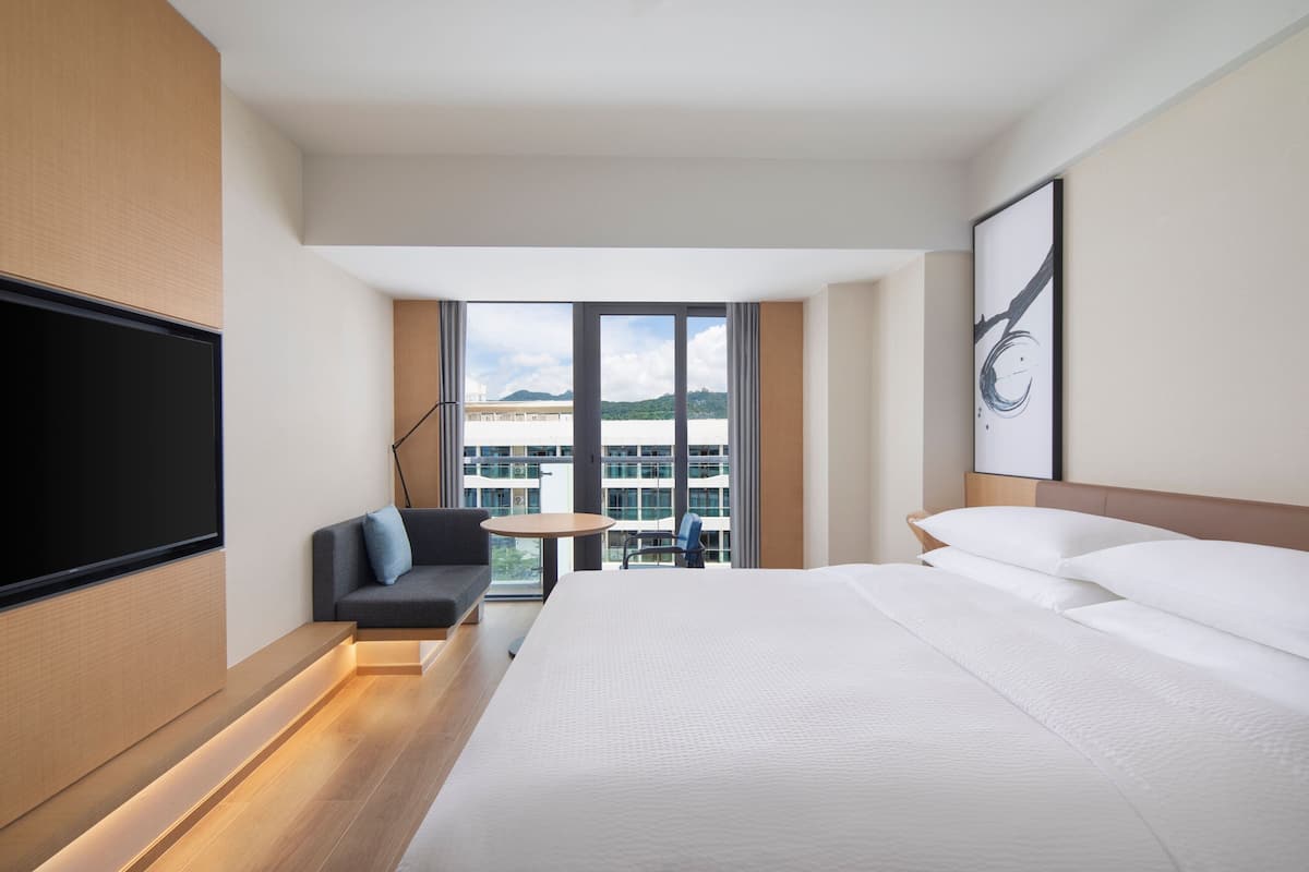 A modern hotel room with a large bed, a sofa, a small table, and a TV.