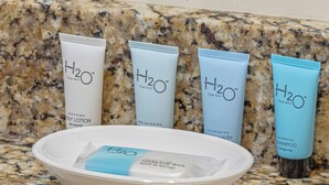 Vier tubes H2O Therapy douchegel en een witte kom met een blauwe handdoek op een granieten aanrecht.
