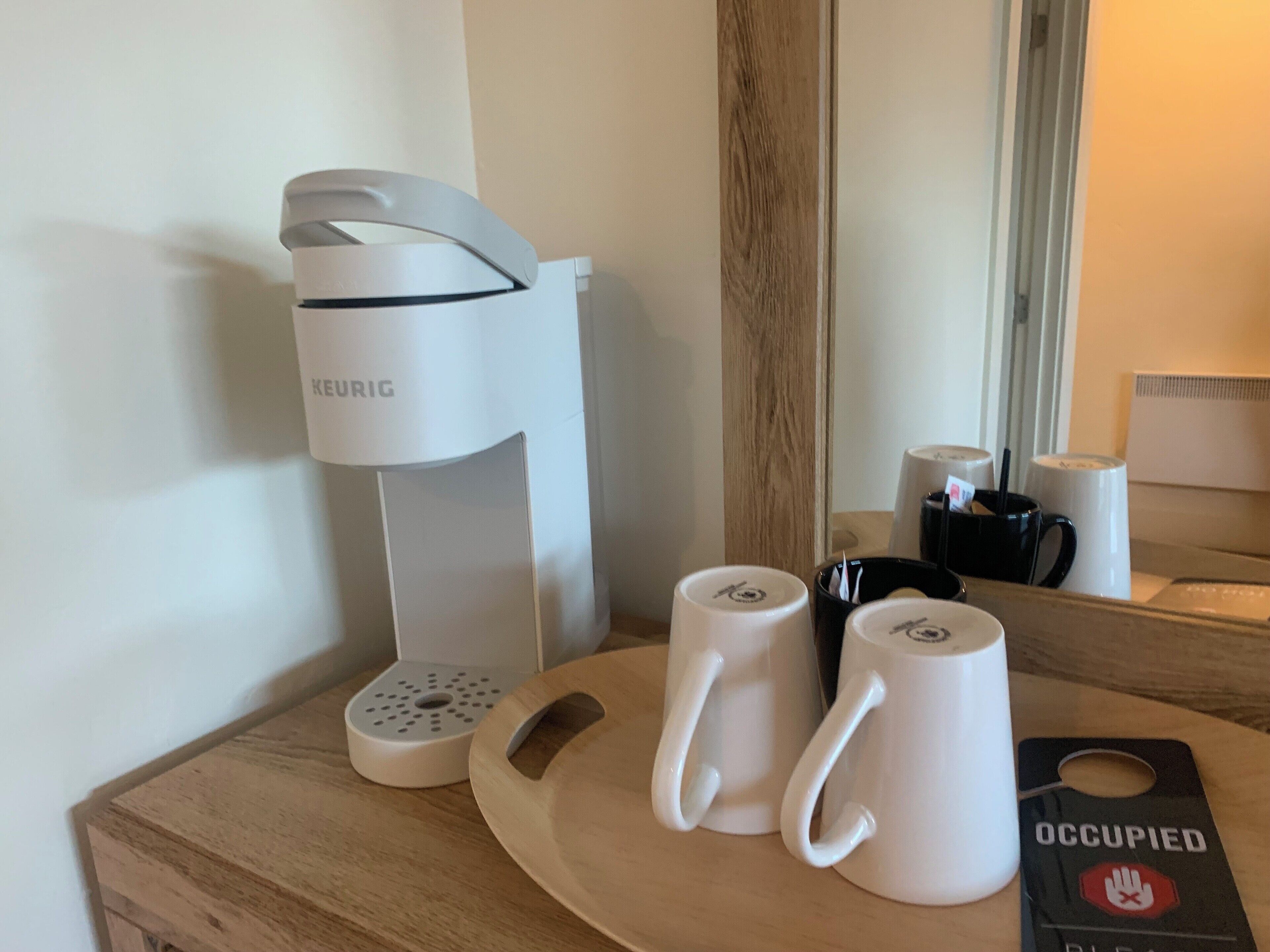 Une machine à café, deux tasses blanches et une assiette avec une étiquette, le tout posé sur une surface en bois.