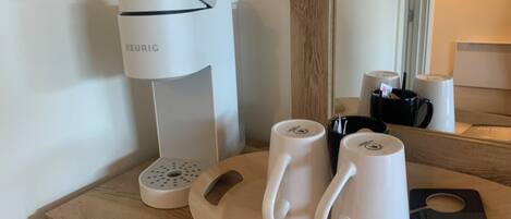 Une machine à café, deux tasses blanches et une assiette avec une étiquette, le tout posé sur une surface en bois.