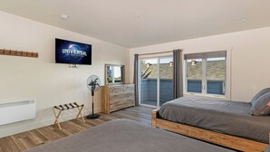A bedroom with a bed, a standing fan, a TV, and a sliding glass door to a balcony. - Downtown Friday Harbor! Newly Built! Shogun Room (Friday Harbor)