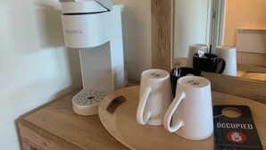 Una cafetera, dos tazas blancas y un plato con una etiqueta sobre una superficie de madera.