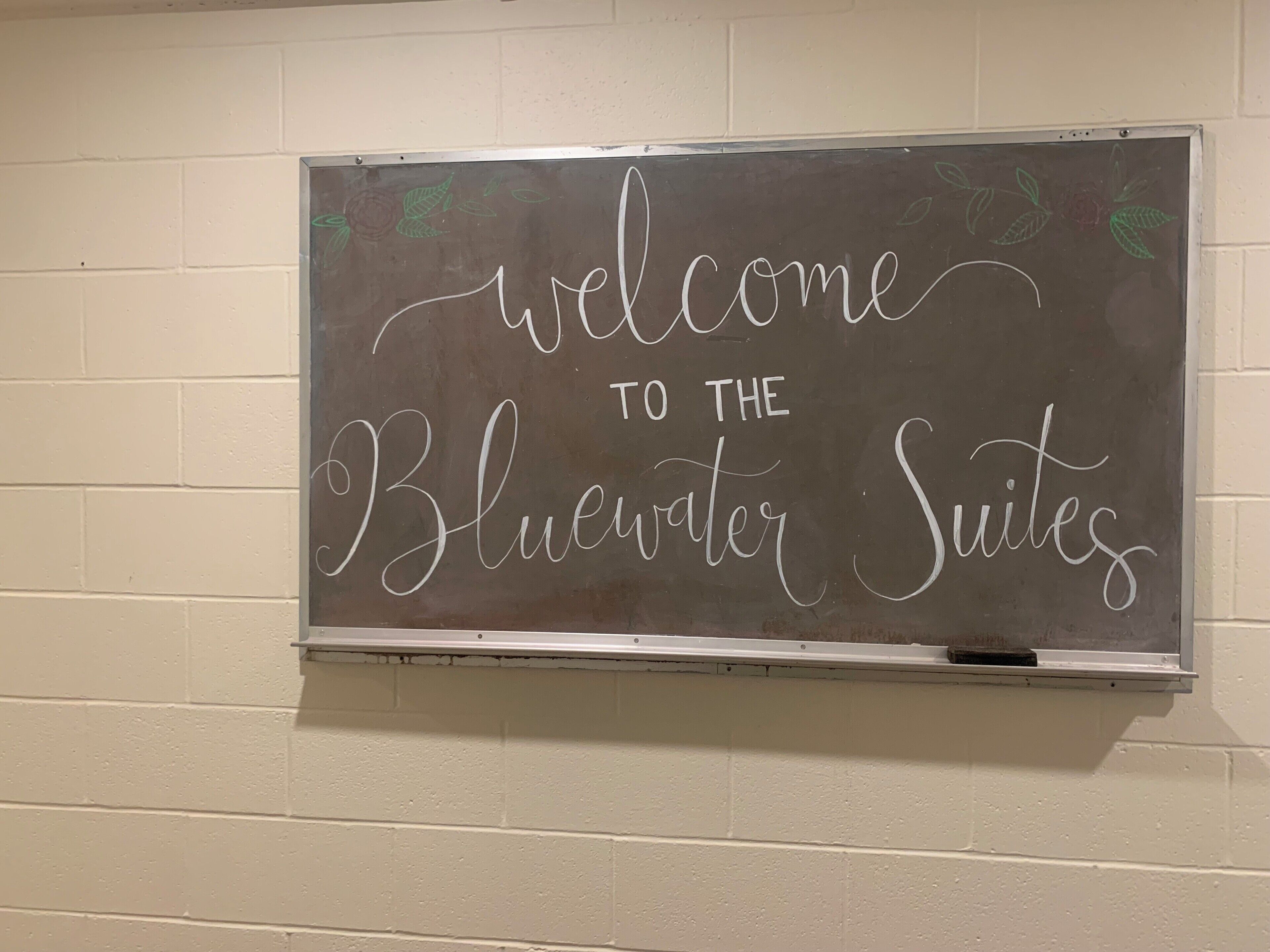 Un tableau noir sur lequel est écrit « Bienvenue à la Bluewater Suites », fixé à un mur de briques blanches.