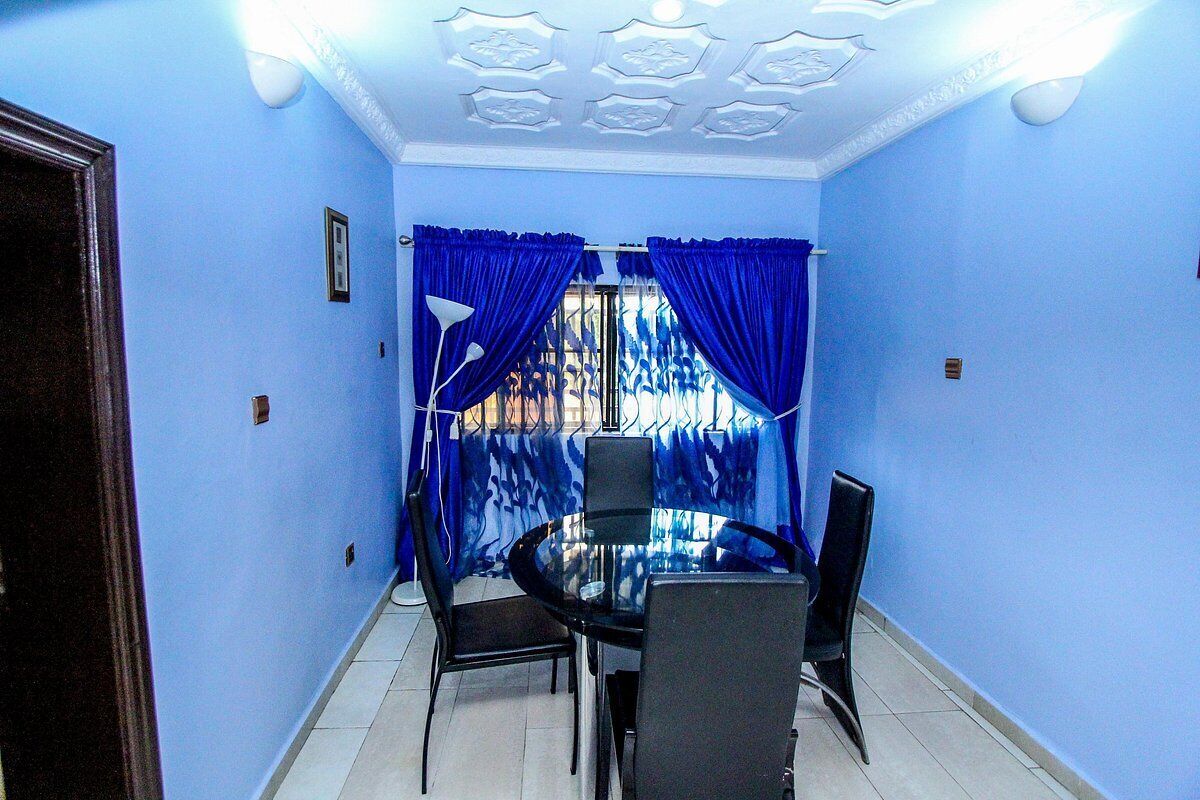 Una habitación con una mesa redonda de vidrio y cuatro sillas, paredes azules y un techo con molduras decorativas.