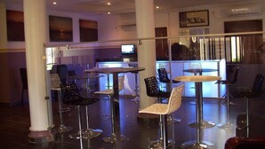 A modern bar area with round tables and chairs, a counter with a computer, and artwork on the walls. - Aaron's Place (Enugu)