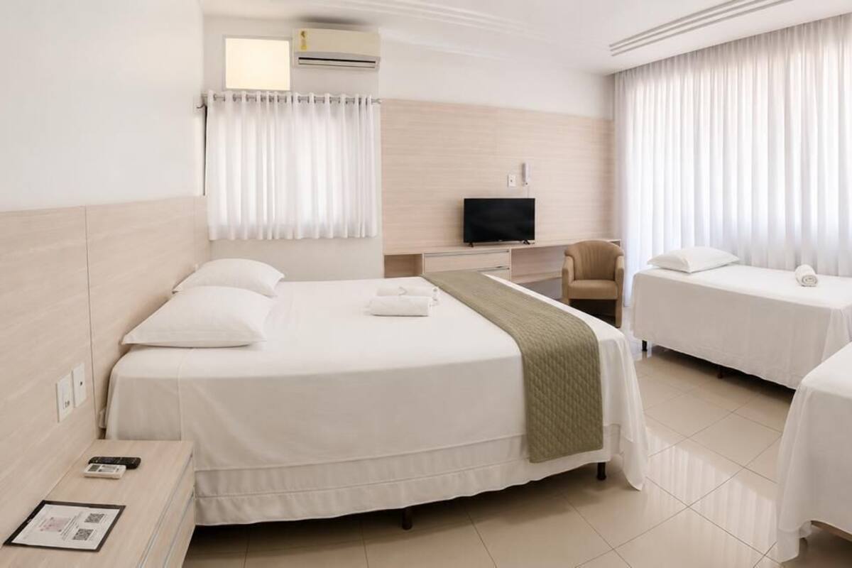 A hotel room with two beds, a desk, a chair, a television, and a window with curtains.