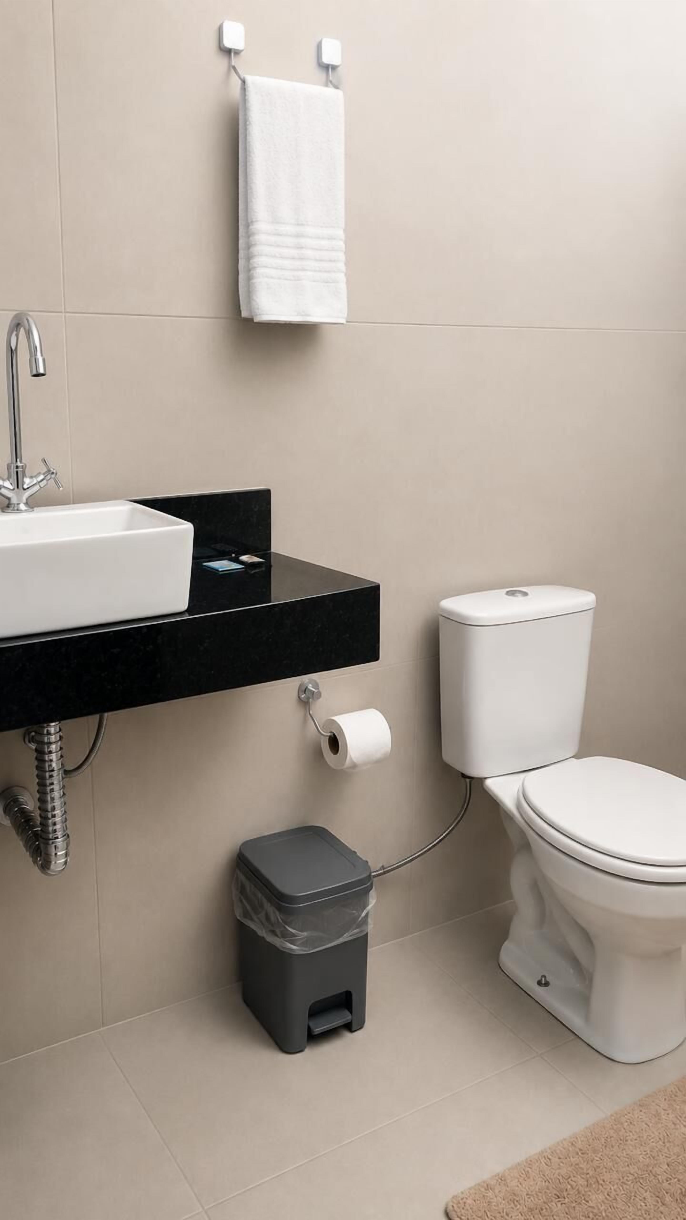 A modern bathroom with a white sink, black countertop, white toilet, and a grey trash bin.