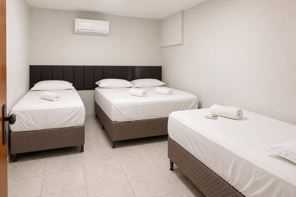 A hotel room with three beds, a wall-mounted air conditioner, and a door.