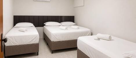 A hotel room with three beds, a wall-mounted air conditioner, and a door.