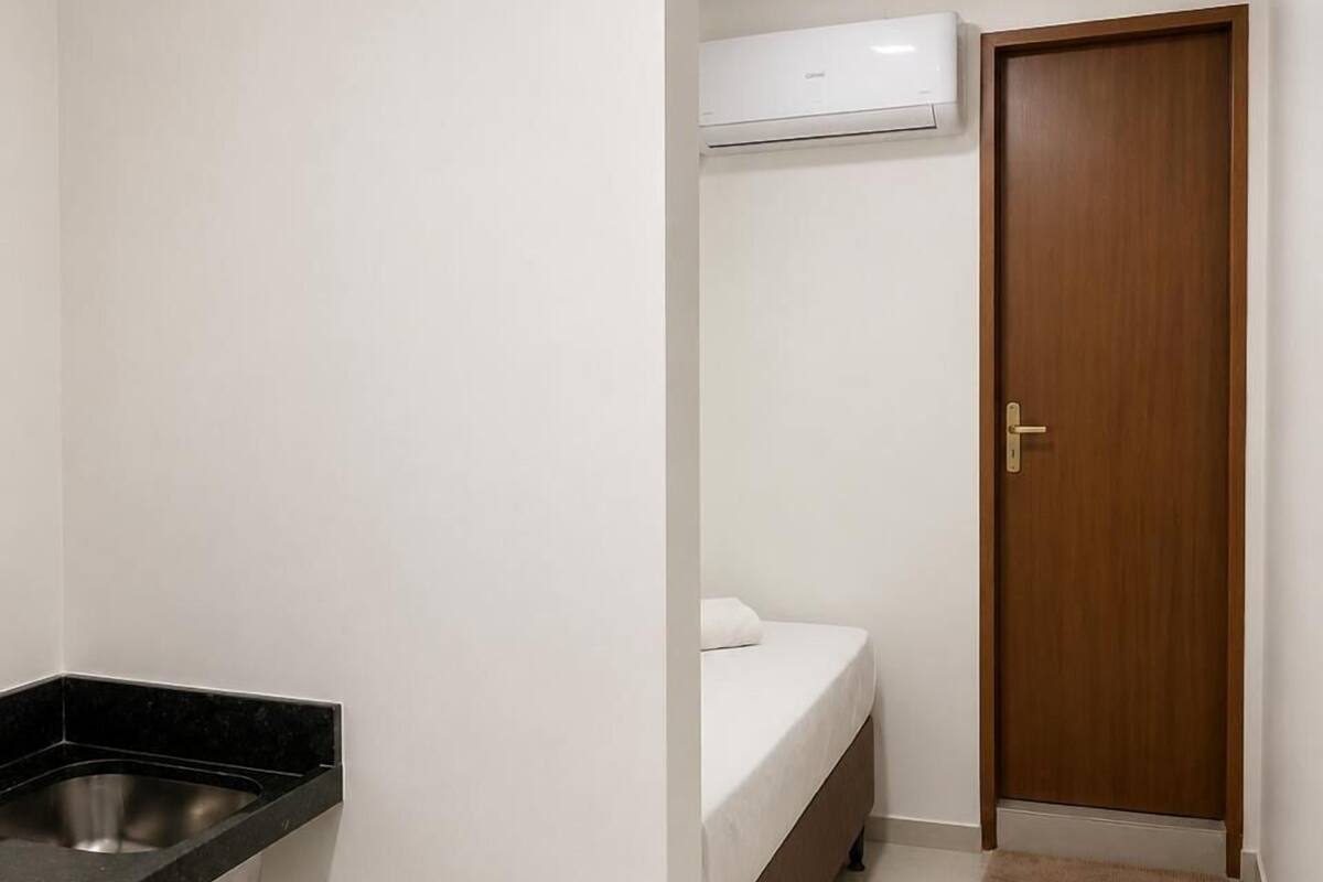 A small, clean room with a kitchenette, a bed, and a door.
